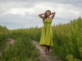 A woman in a green dress standing in a lush field under cloudy skies.